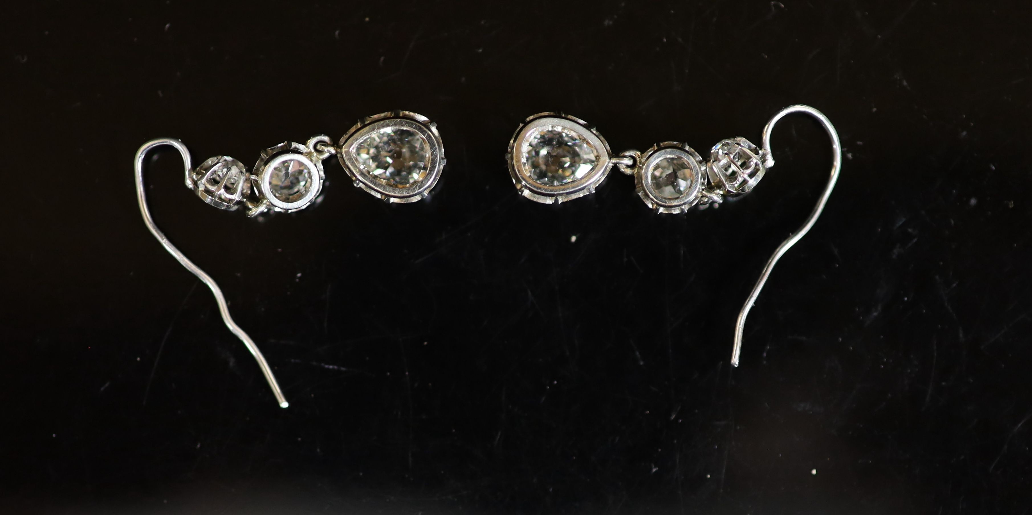 A pair of white gold, and graduated illusion set three stone old round and pear cut diamond drop earrings